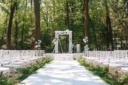 A flower wedding arc stands in the nature in a park on a sunny day. Front view with chairsの写真素材