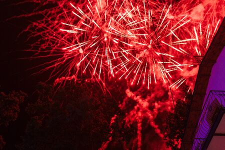 Explosions of red fireworks on the background on a dark night sky and hotel balconyの写真素材
