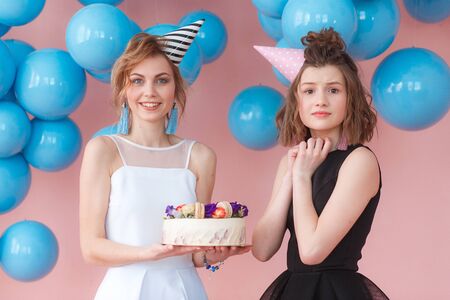 Two teenage girls holding birthday cake. Wearing black and white dresses and hatsの写真素材