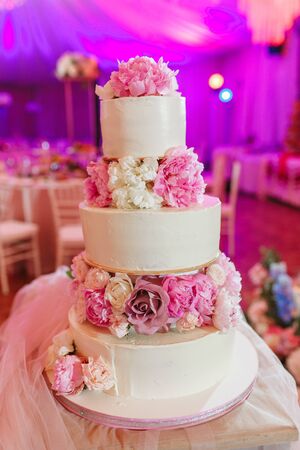White wedding cake decorated with peony roses on pink restaurant backgroundの写真素材