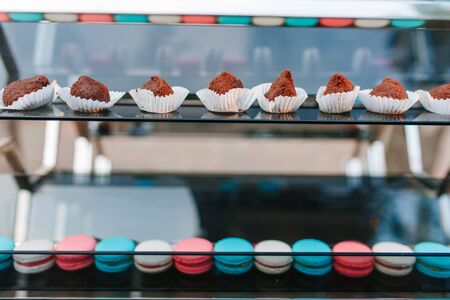 Two color macaroons and chocolate cakes on glass display shelvesの写真素材