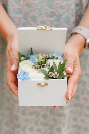 Woman holding wedding rings in wooden box decorated with flowers. Close horizontal photoの写真素材