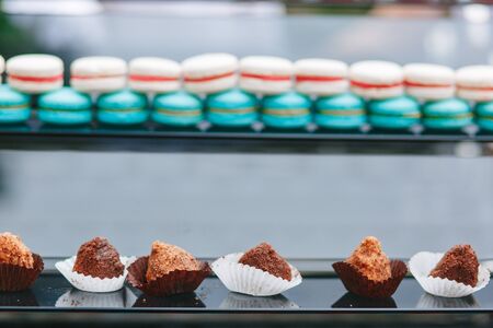 beautiful chocolate small cakes at glass shop-window with colorful blurred macaroons on backgroundの写真素材