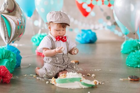Baby boy touching his first birthday cake. Making messy cake smash in decorated studio locationの写真素材