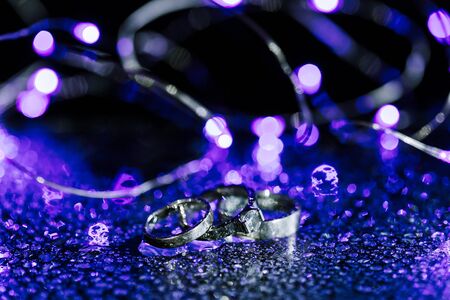 Classic white gold wedding rings close-up on wet sparkling background. Monochrome copy space photo.の写真素材