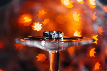 Diamond gold Engagement ring in sparkling orange light leaves decoration on glass bottom.の写真素材