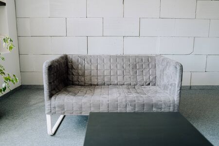 Sofa Modern Textile Grey Upholstery Room Element with Foam Brick Wall on Background Copy Space. Elegant Fabric Couch and Black Table on Gray Carpet Covering Floor. Office Stylish Interiorの写真素材