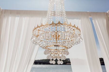 Crystal Balls on Golden Chandelier and Altar Arch with White Curtains, Blue Sky, River and Forest on Background Horizontal Photo. Altar Decoration Closeup. Wedding Day Place for Romantic Ceremonyの写真素材