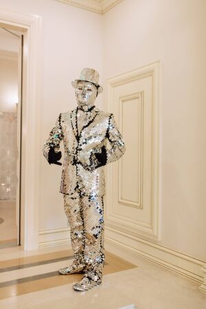 Man in Bright Performance Mirror Costume and Hat. Mirrorman Male Wearing Decorative Suit and Cap in Broken Glass Style Staying in Disco Party Room. Living Statue Vertical Photographyの写真素材