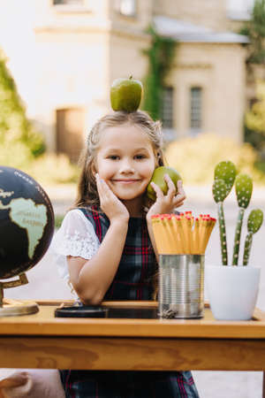 Happy Primary Girl Sit At Desk Hold Apple on Headの写真素材