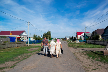 three people walk along the road in the village against a beautiful skyの写真素材