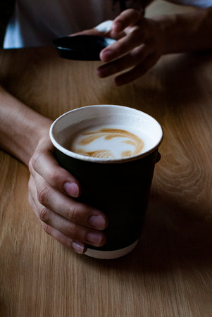 the green paper cup with coffee stands on a wooden table in a persons handの写真素材