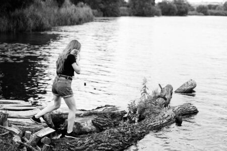 A young woman walks with a three month old Scottish Reed kitten near the lake in summer. The black-and-white photo was taken in the general plan in sunny weather with natural lightの写真素材