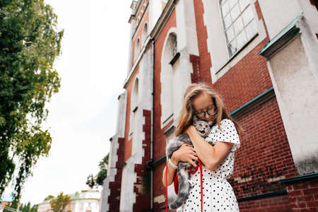 Young blonde girl holds in her arms and hugs lovingly her pet domestic kitten breed Scottish Straight in the cityの写真素材