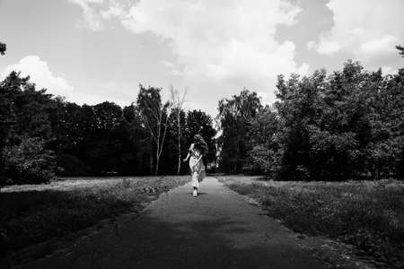 Woman in a long white dress walks with a pet kitten breed Scottish Straight in the park in summerの写真素材