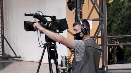 Young male videographer in a protective medical mask filming a city event during coronavirus...