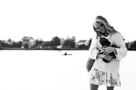 Young blonde girl with glasses holds a cat breed Scottish Straight. Walk with pet near the lake, river at sunset on the beachの写真素材