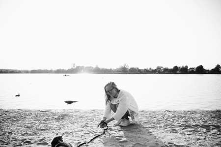 Young blonde, woman, girl on the beach in spring in a white knitted sweater and dress with a Scottish Straight cat on a sunny day on a picnicの写真素材