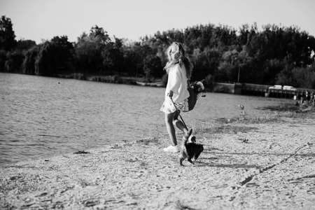 Young blonde, woman, girl running on the beach in spring in a dress and white sweater with a cat on a sunny dayの写真素材