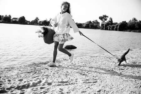 Young blonde, woman, girl running on the beach in spring in a dress and white sweater with a Scottish straight cat on a sunny dayの写真素材