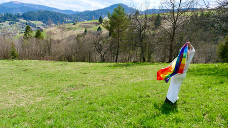Woman blonde with  rainbow flag in mountains on nature in white dress. A happy bride of...