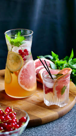 Grapefruit lemonade with mint, lemon, currants and ice in a decanter and a glass with black plastic...