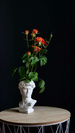 Orange rose bush flower on isolated black background in original vase sculpture of David. Gift for a woman, mother, grandmother, wife on March 8, Womens Day, Mothers Day, birthday, Valentines Dayの写真素材