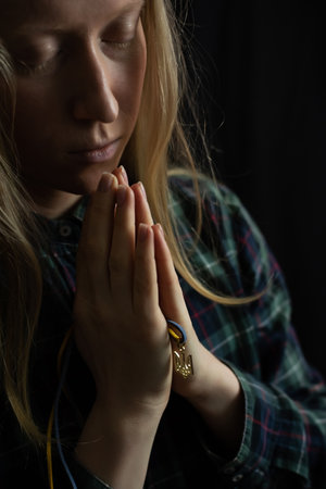 Ukrainian blonde woman prays for Ukraine during the war with the national emblem Trident in the palms close up. Russia attacked Ukraine on February 24, 2022の写真素材