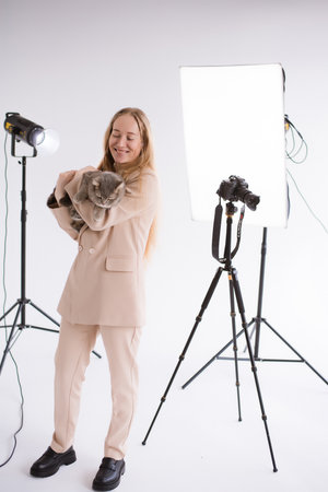 A business woman, freelancer, blogger in suit is working on a white floor, black background. blonde assistant in video production with camera and scottish straight catの写真素材