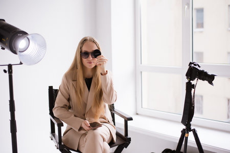 A woman videographer in sunglasses, a blonde with a camera on a tripod in the studio. Wearing a...