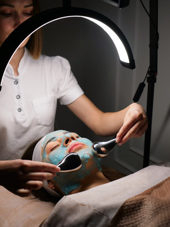 Cosmetologist does cryo massage with globules on a blue hydrogel alginate mask in the beauty salon, vertically, close-up. Woman Facial Skin and Body Careの写真素材