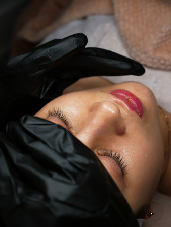 The beautician performs the procedure of microcurrents in black electric gloves to restore facial...
