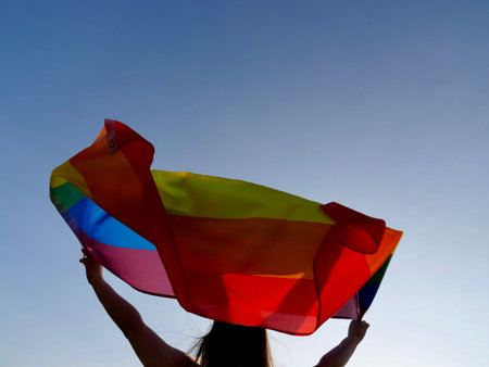 Rainbow flag of an LGBT organization waving against a blue sky. LGBT pride flags include lesbians, gays, bisexuals and transgender diversity people.の写真素材