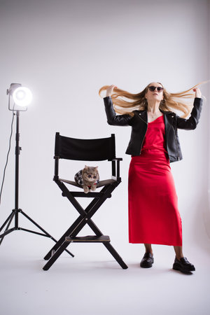 A woman, freelancer, blogger in a silk red dress on a white floor, black background. blonde owner cat of the Scottish Straight breed at studioの写真素材