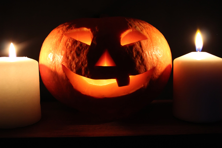 Funny smiling glowing halloween pumpkin (Jack-o'-lantern) and candles lights on black backgroundの写真素材