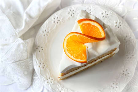 a piece of orange cake with whipped cream decorated with a slice of orange on a white backgroundの写真素材