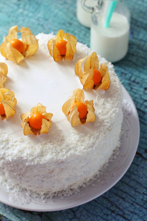 homemade cake, covered with cream and decorated with winter cherry and coconut, closeup on a blue backgroundの写真素材