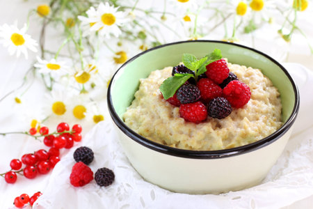 Oatmeal with raspberries and blackberries and mint in a bowl on a white background, chamomile in the backgroundの写真素材