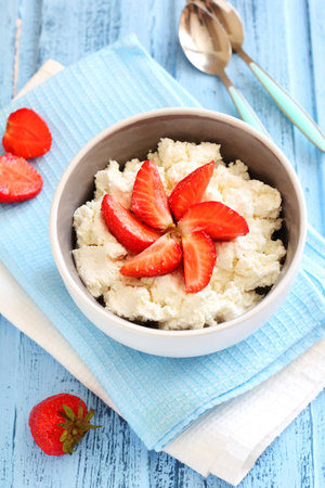 Breakfast with cottage cheese with strawberries in a ceramic bowl on blue boards, top viewの写真素材