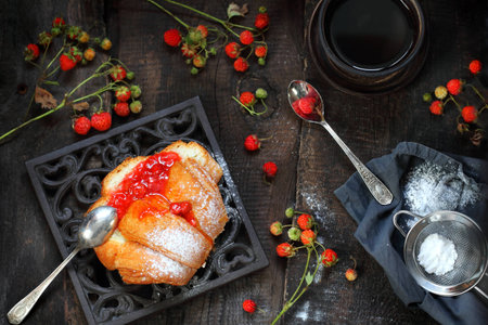 bun with homemade strawberry jam and black coffee on a wooden backgroundの写真素材