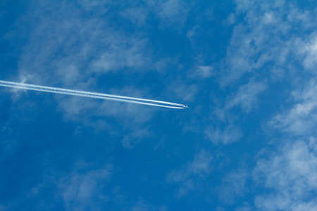 Airplane in flight with exhaust tail against the blue sky with cloudsのeditorial素材