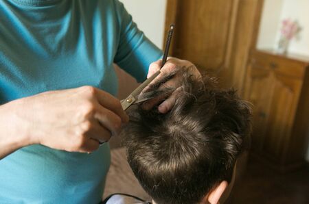 Home haircut during quarantine. The best master is mother's hands, scissors and a trimmer.の写真素材