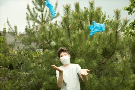 The joy of a young man in the nature after quarantine. Soon a mask and gloves will not be needed. The boy takes off and throws out the gloves.の写真素材
