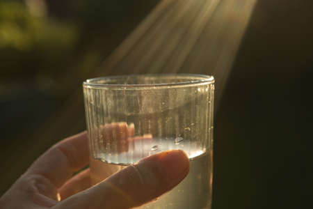 The sun's rays are caught in a glass of water. A glass in the hand of a man in the sunset sun.
