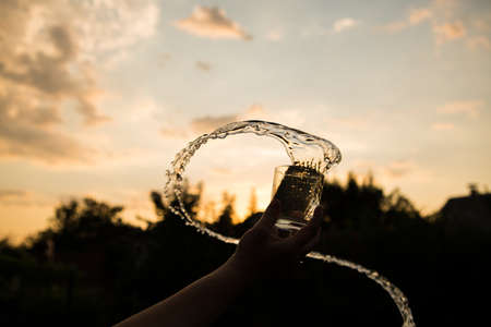 Splash of water in a glass. Flying water. A glass of water in a man's hand in the sunset.の写真素材
