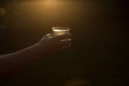 A glass of water in the human hand in the sunset. Life during a pandemic.の写真素材