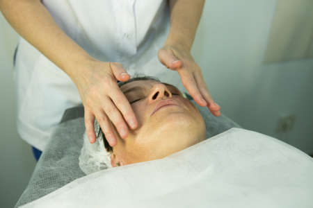 A visit to the beautician. Procedure-carboxytherapy. Doctor cosmetologist makes facial massage of the patient after the procedure.の写真素材
