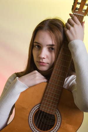 Portrait of a young girl with a guitar. Emotion concept. Photo on a pink-yellow background in neon...