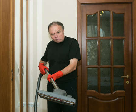 Emotions of a middle-aged man before cleaning an apartment. Daily cleaning of the premises. Humor. A man holds a vacuum cleaner in his hands.の写真素材