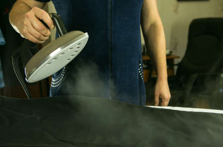 Homework. Woman ironing linen with a steam iron. The steam jet is clearly visible in the photo.の写真素材